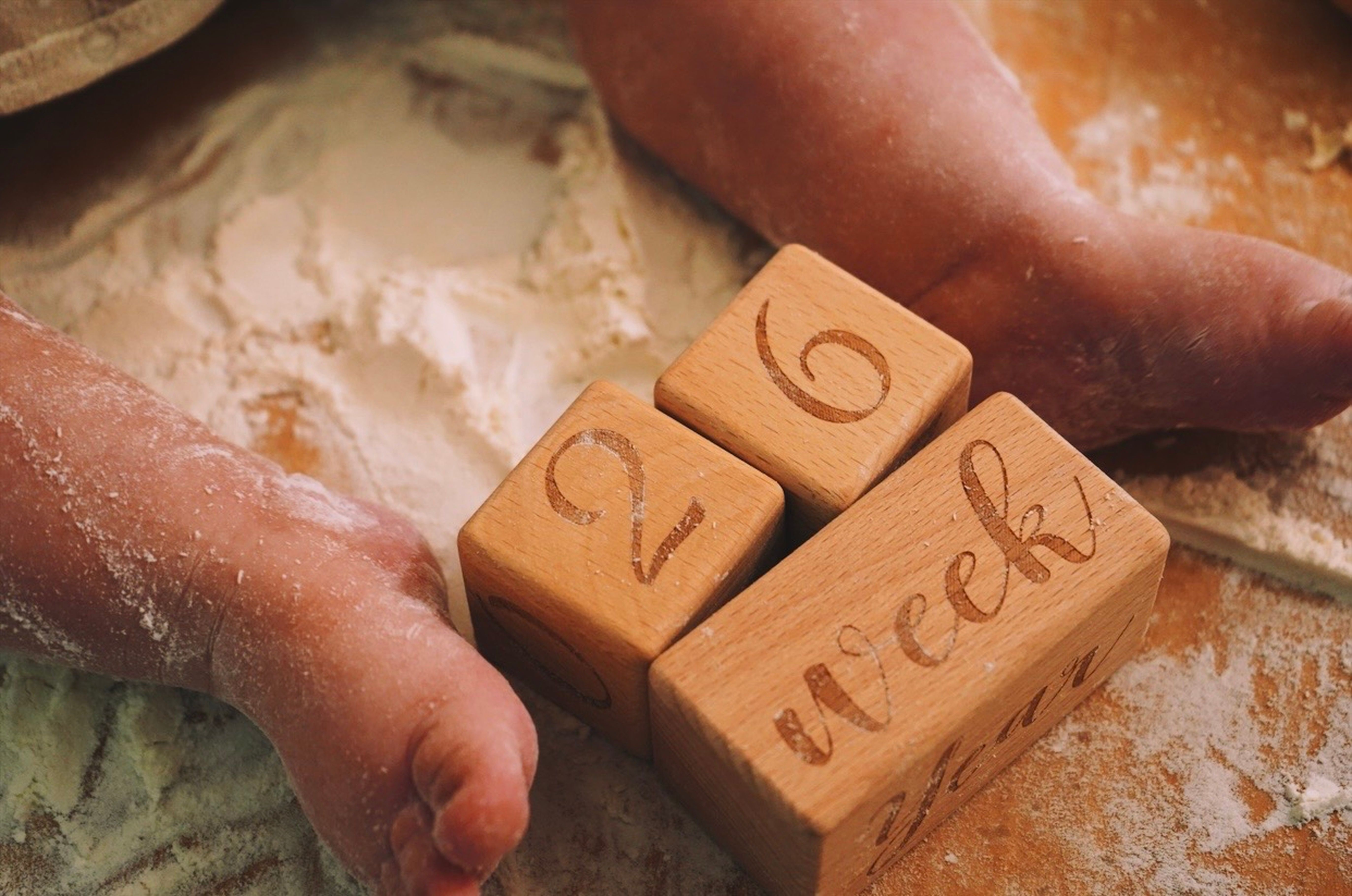 Baby feet beside wooden milestone blocks showing 26 weeks, a visual example of recording baby milestones.