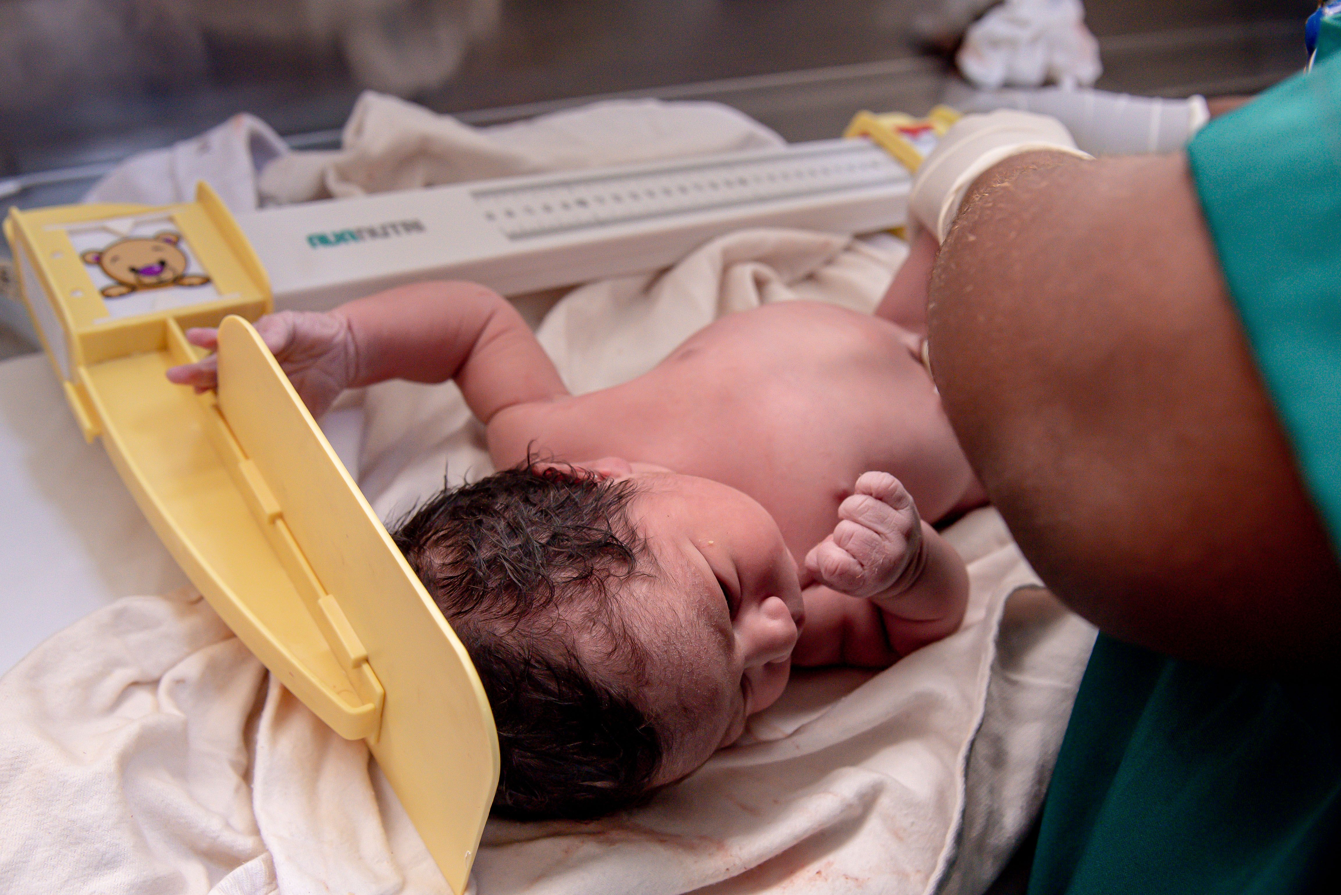 Newborn being weighed by a healthcare worker, representing baby weight and physical growth tracking.