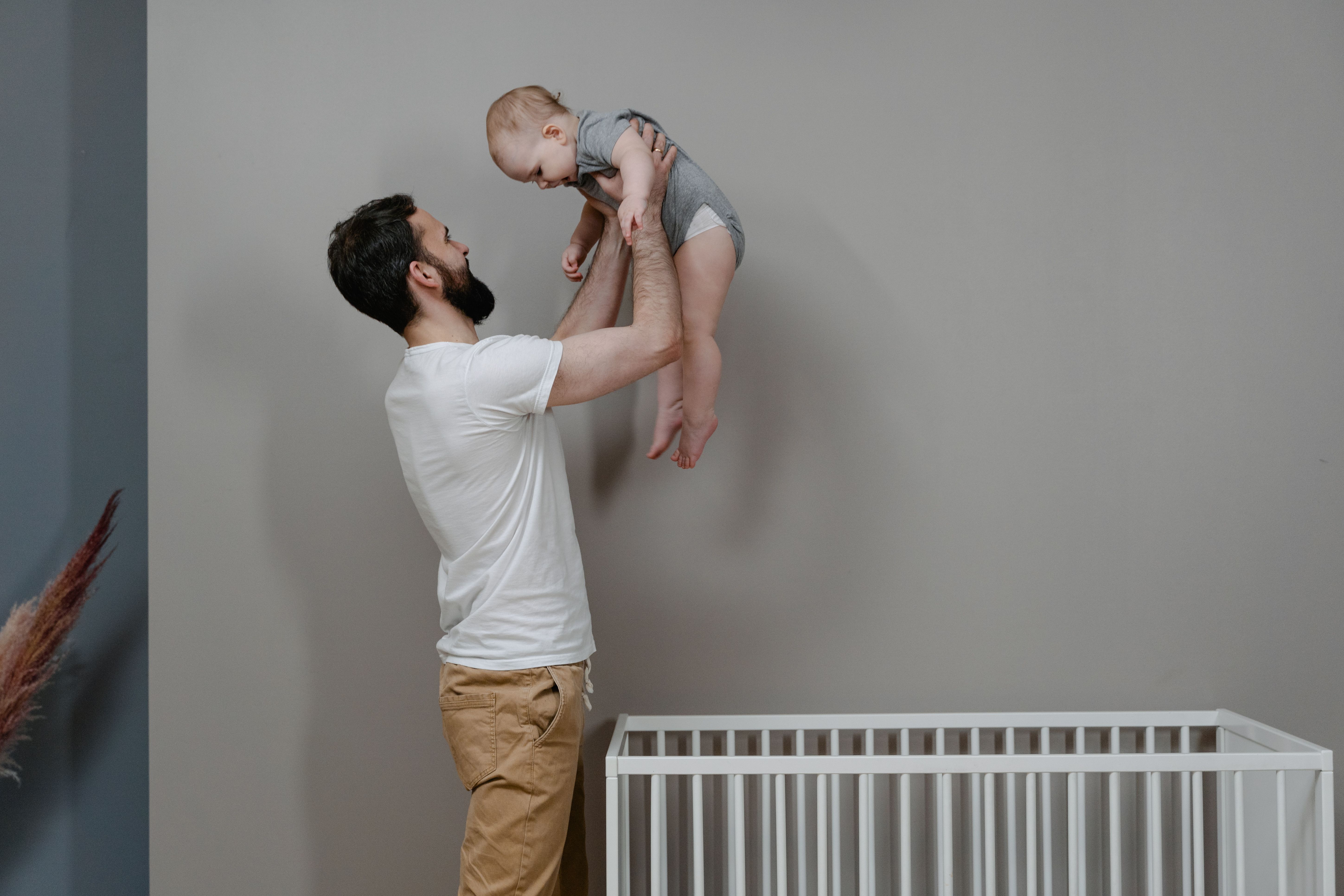 Parent lifting a baby near a crib, capturing a family moment to include in a visual growth chart.